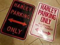 Photo showing two Harley Davidson parking signs on a tiled floor, one black metal and one white plastic.