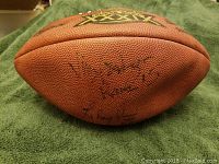 Close-up of the Wilson football showing multiple autographs in black marker, ball partially deflated with visible wear.