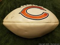 Full view of the white football showing the Chicago Bears 'C' logo on one side, lying on a green fabric background.