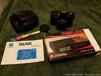 1980s Pentax Talker camera with broken lens cap, camera manual, colored marker pen, and Enterpax travel clock radio in original box.