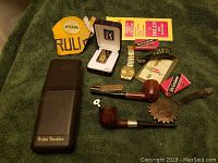 Overview photo of the lot including PGA patch, Seiko watch, tobacco pipes, Pocket Traveler case, and associated items on a green fabric background.