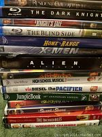 Photo showing 15 movie discs in cases, including 4 BluRay and 11 DVDs. Visible movie titles on case spines. Cases show visible wear and surface scratches on discs possible.