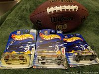 Wilson Pro football and three Hot Wheels cars in original packaging on green fabric background.
