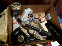 Box containing assorted miscellaneous items including thermometer in box, masks, goggles, and small tools