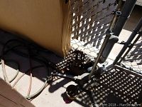 Photo of metal reel with black cable, some pipes, and metal rods near a cardboard box and chain link fence.
