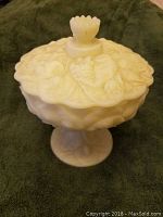 Front view of white milk glass candy dish showing pedestal base and lid with detailed fruit and leaf pattern.