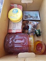 Top view of the cardboard box containing various items including carnival glass jar, Ritz Bits tin, vintage Butter box, small decorative items and postcard.