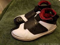 Side angled view of used white Nike Air Jordans with black embossed strap and red interior, showing wear