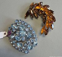 Both brooches side by side showing overall designs and stone colors