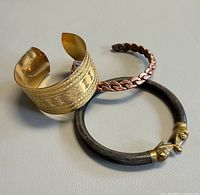 All three bangles grouped: engraved cuff, braided copper bangle, patinated bangle with animal heads