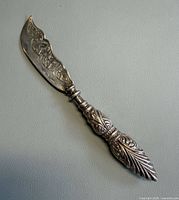 Full view of ornate sterling butter spreader front side showing chased floral blade and repousse handle