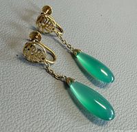 Full view of both earrings showing gold screw backs, Chinese character discs, chains and green teardrop stones