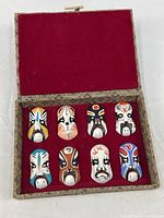 Open box showing eight miniature masks mounted on red fabric