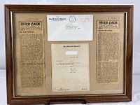 Overall view of framed display showing two newspaper clippings, envelope, and typed note