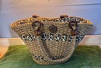 Front view of woven straw tote showing leopard print panels, rope handles, wood rings