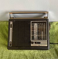 Front view showing tuning dial, speaker grille, carry handle, brand name