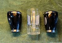 Front view of two black travel mugs and clear glass beer stein