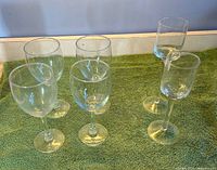 Six clear stemmed glasses on green surface