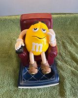 Front view of Yellow M&M dispenser in chair on patterned base