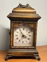 Front view showing clock face, wooden case, metal feet