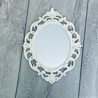Full view of ornate white oval wall mirror on gray background