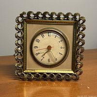 Front view of square gilt clock with cream dial and filigree frame