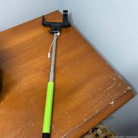 Full view of telescoping selfie stick showing green handle, silver rod, and black phone holder