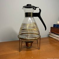 Full view of Pyrex glass carafe on metal stand showing gold trim and handle