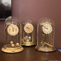All three brass anniversary clocks under their glass domes