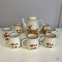 full set: coffee pot with lid plus seven mugs, pattern visible