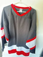 Front view of grey hockey jersey with red collar and red/white stripes