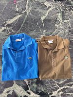 Blue and brown Lacoste polo shirts folded side by side showing front and logos