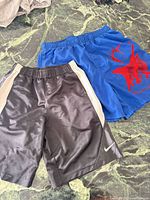 Black Nike shorts with grey panels and blue Guy Harvey shorts on green surface