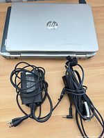 HP laptop closed with both power adapters on wooden surface