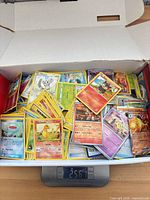 Open box on scale reading 2567 g showing large quantity of Pokémon cards