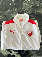 Folded jacket front showing crest, Puma logo, red shoulder panel