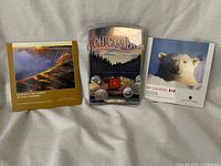 Front view of the three Oh! Canada coin sets: 1998 booklet, 2005 acrylic case, 2006 booklet