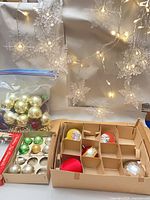 Bag of plastic ornaments, tray of vintage ornaments, lit snowflake string lights backdrop