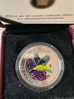 Colourized 25-cent goldfinch coin in capsule inside black felt insert