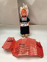 Full view of doll seated with wrapper in front