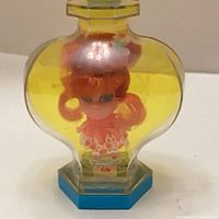 Front view of perfume-shaped bottle showing doll and hexagonal base