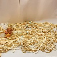 Pile of gold and white bead strands with Christmas corsage arranged on neutral background