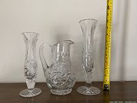Two pinwheel cut crystal bud vases and creamer with tape for scale