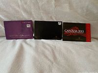 Three closed presentation folders for 2003, 2007 and 2013 uncirculated coin sets
