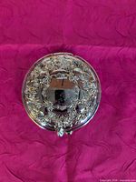Closed compact mirror showing ornate floral silver-plated lid