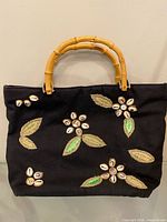 Full view of black tote showing shell and raffia flower designs