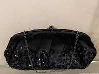 Front view of black satin clutch showing sequined lower half and chain strap
