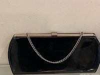 Front view of black patent leather clutch purse with chain strap displayed against plain background