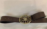 Full view of brown leather belt laid flat showing buckle and strap