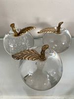 Three clear glass apple paperweights with brass stems